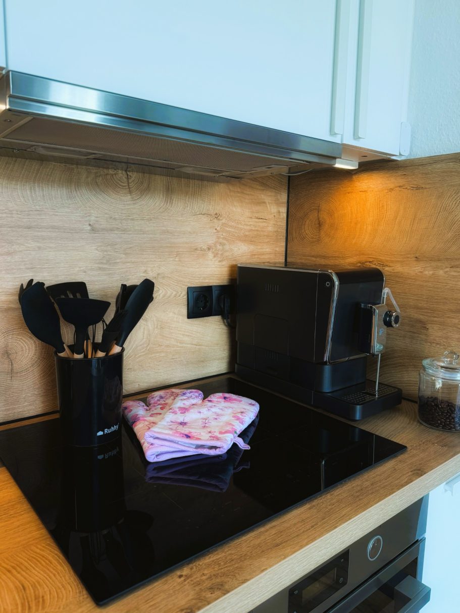 Schwarze Kochutensilien, ein Kaffeekocher und ein Geschirrtuch auf einer modernen Küchenarbeitsfläche.